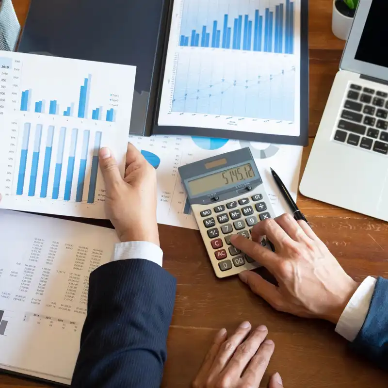 Two businessmen running numbers with a calculator and spreadsheets.