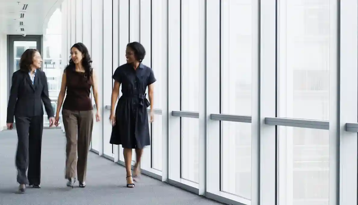 Three women converse as they walk along a hallway.