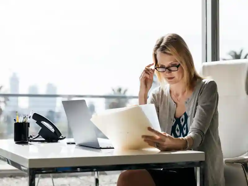 Businesswoman reading documents while sitting at desk in office.