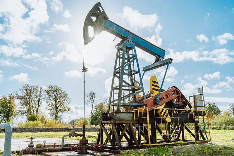 A pump jack with bright sunlight behind.