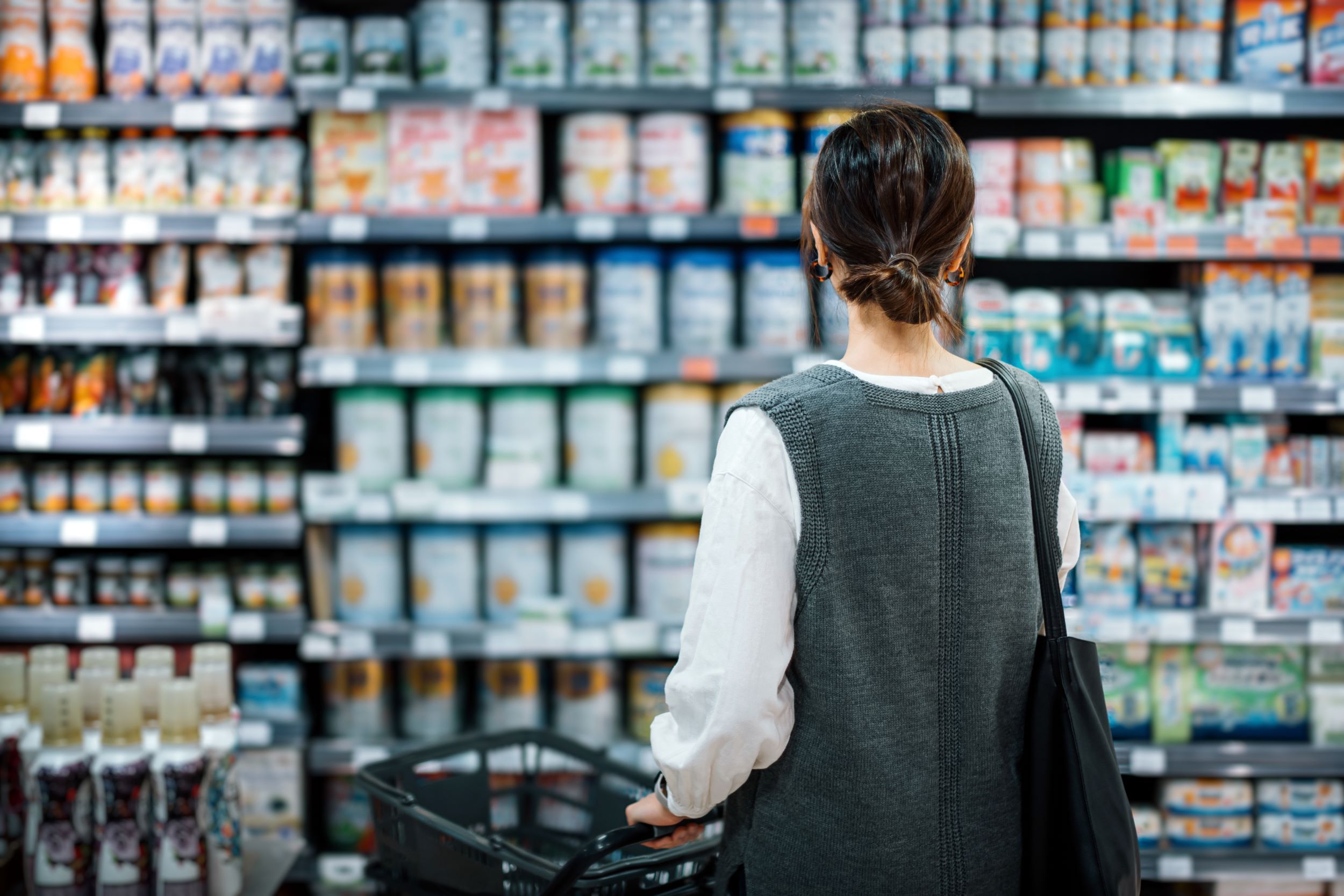 Woman standing in of stocked shelves in a grocery store.