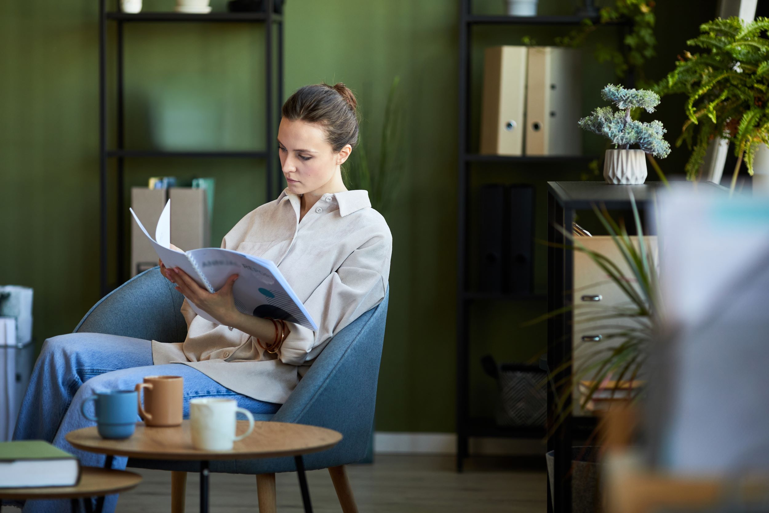 Woman sitting in a chair in a modern waiting room reading a magazine.