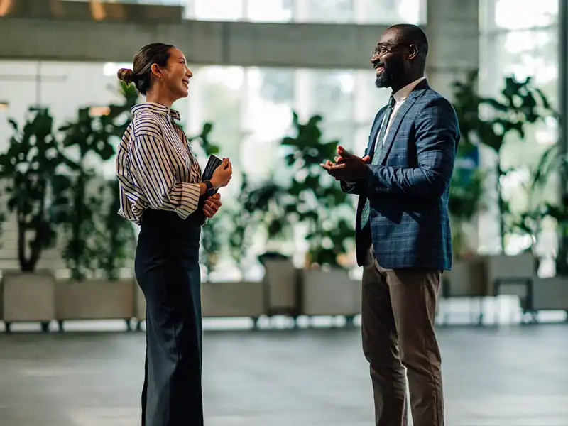 Two business professionals converse in a large lobby.