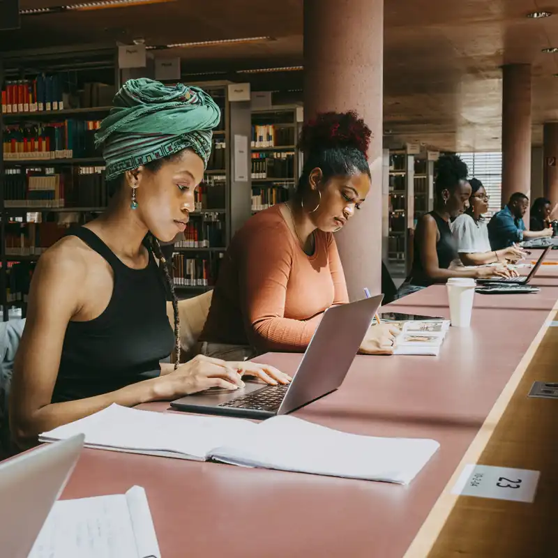 People study various subjects at a long table in a library.