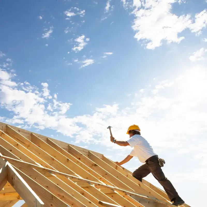 Male roofer carpenter working on roof structure on construction site.