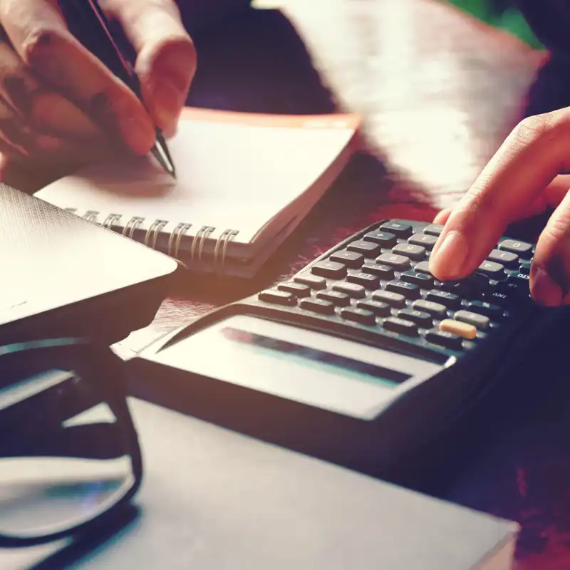Close up woman hand using calculator and writing make note with calculate about cost at home office.