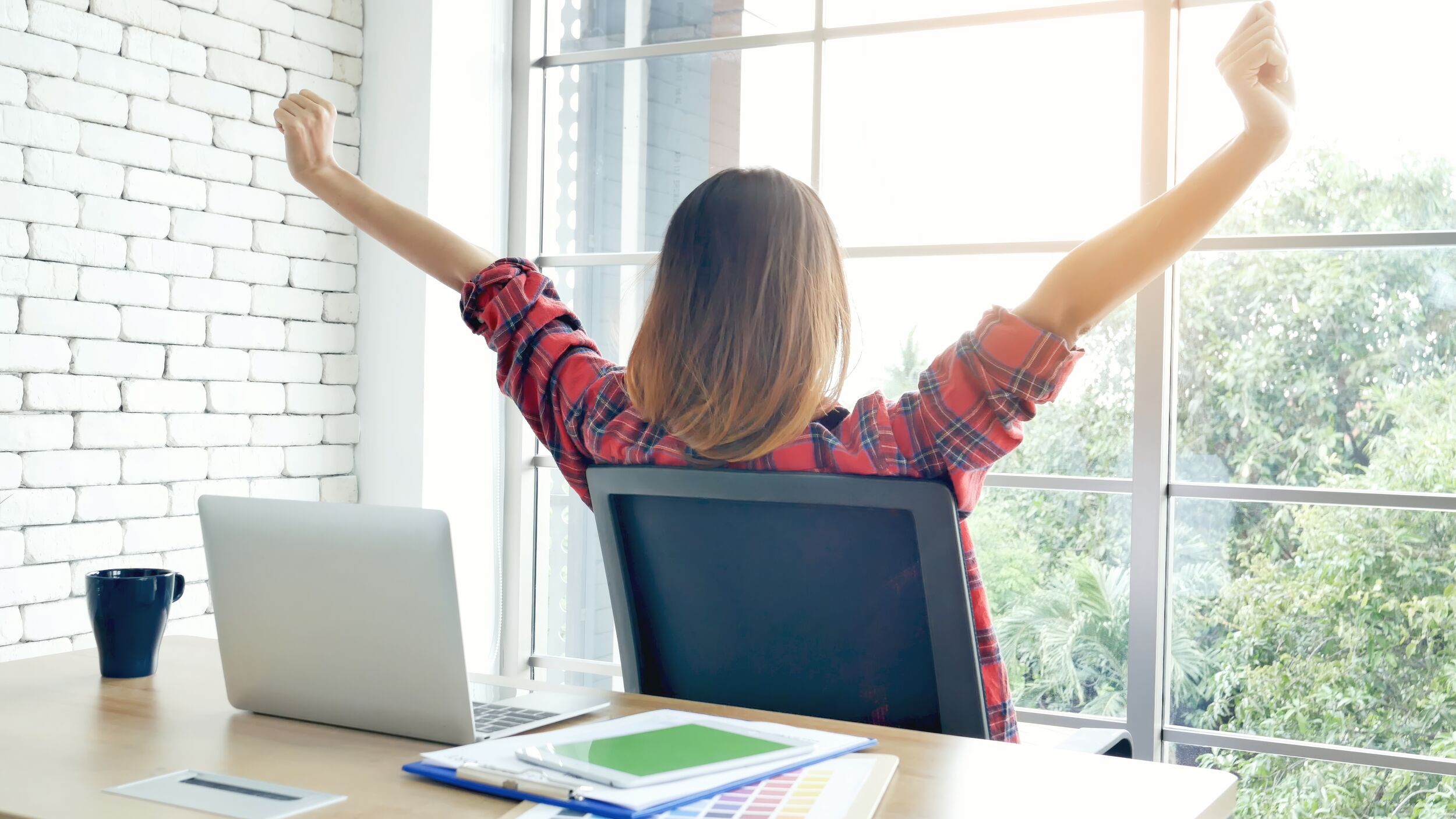 Woman stretching arm raised sitting incorrect position home office desk.