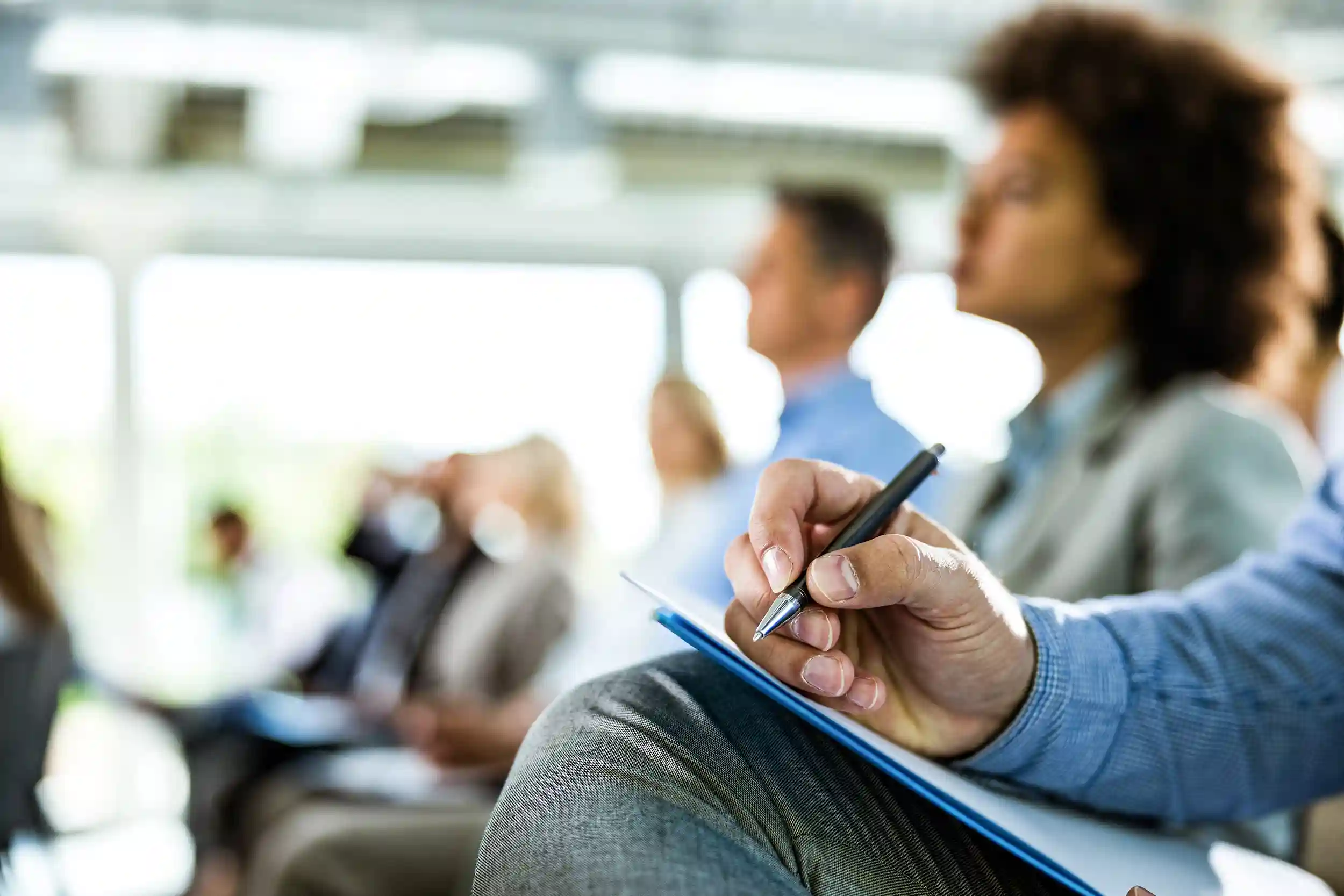 close up of a man holding a pen and notebook at a business conference