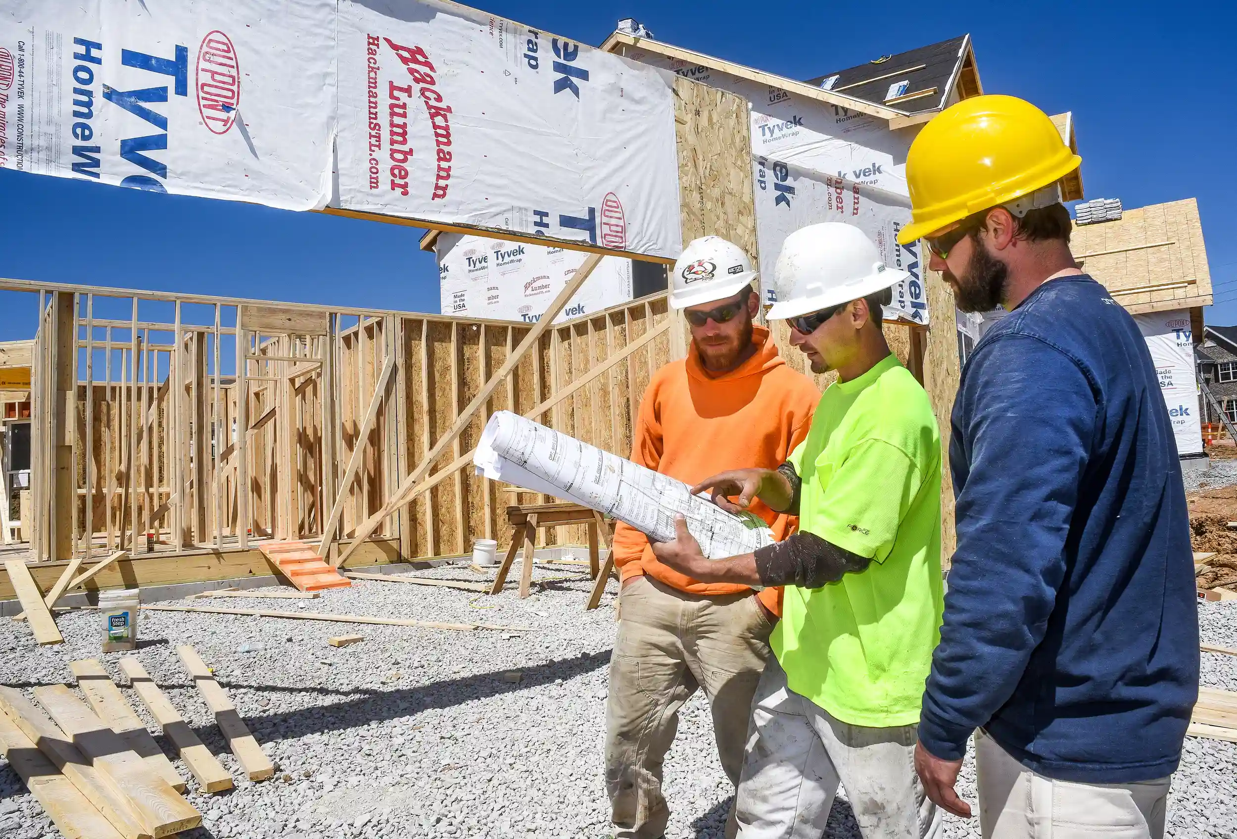 Three male construction workers, carpenters, wearing hardhats looking at blueprints.